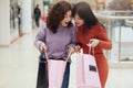 Horiontal shot of two beautiful women looking inside their shopping bags and admiring purchases, brunette girls posing with opened