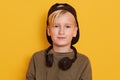 Horixontal shot of little blond boy with headphones around neck, male child listening to music via headphones, wearing green shirt Royalty Free Stock Photo