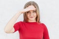 Horizonntal portrait of pretty blonde female with freckles, blue charming eyes and dimples dressed in red sweater holding hand on