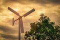 Horizontal axis wind turbine with blue sky and white clouds near green tree. Wind energy in eco wind farm. Green energy concept. Royalty Free Stock Photo