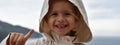 Horizontal banner or header with a little smiling girl wearing a raincoat jacket with hood against the stormy sky - She lifts her Royalty Free Stock Photo