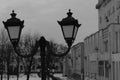 Horizontal black and white photo of an old street lamp in a cityscape with a blurred background on a cloudy winter day. Royalty Free Stock Photo