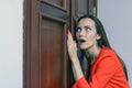 Horizontal close-up portrait of a woman in a red suit eavesdropping, spying on the door of the boss Royalty Free Stock Photo