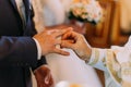 The horizontal close-up view of the priest putting on the groom golden wedding ring at the background of the church.