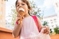 Horizontal closeup portrait of cute little girl walking along city street and eating ice cream outdoor. Happy kid girl wears pink Royalty Free Stock Photo