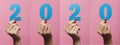 Horizontal collection of female hands holding and showing date 2020 cut out of cardboard on a colored pink background, concept new