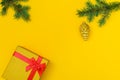 Horizontal festive yellow background: shiny gift box with red ribbon, fir branches and Christmas tree toy - golden cone.