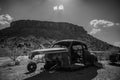 Horizontal greyscale shot of a destroyed classic car near a beautiful mountain on the Route 66