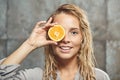 Blonde caucasian female model with a piece of orange near her face, close up shot in the bathroom.