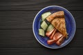 Horizontal image of vegetable pie with spinach and salmon on blue plate from above on a textured black background