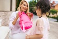 Horizontal image of happy amazed mother preparing backpack to put on backpack to her kid to going to kindergarten outdoor. Cute