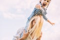 Horizontal image of happy little daughter on a piggy back ride with her smiling mother on sky background. Loving woman and her