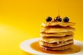 Horizontal image of maple syrup pouring onto pancakes and blueberries, on yellow with copy space Royalty Free Stock Photo