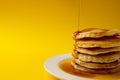 Horizontal image of maple syrup pouring onto stack of pancakes, yellow background and copy space Royalty Free Stock Photo