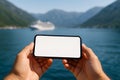 Horizontal image of a smartphone in landscape orientation with blank screen held in front of a distant cruise ship Royalty Free Stock Photo