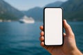 Horizontal image of a smartphone in landscape orientation with blank screen held in front of a distant cruise ship Royalty Free Stock Photo