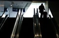 Three large escalators with a silhouette of a man in a business suit carrying a suitcase riding up on one of them