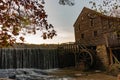 Horizontal image of the waterfall and wooden building and waterwheel at the historic Yates Mill County Park at sunset in autumn