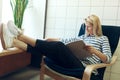 Horizontal image of young beautiful blonde woman sitting on comfortable chair and reading news magazine in the office. Caucasian Royalty Free Stock Photo