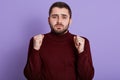 Horizontal indoor photo of hopeful energetic handsome raising hands, clenching fists, wearing dark red sweatshirt, looking