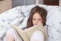 Horizontal indoor picture of curious interested busy infant spending free time alone, reading attentively, studying, lying in