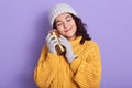 Horizontal indoor shot of tender peaceful young brunette closing eyes, smiling, holding thermomug, putting it close to face, Royalty Free Stock Photo