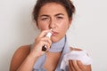 Horizontal indoor studio shot of bad looking woman having caught cold, feeling unwell, being on sick leave, using nose spray,