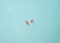 Horizontal minimalistic close-up flat lay composition of red paper clip and stationery button on a light blue background Royalty Free Stock Photo