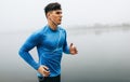 Horizontal outdoor image of young runner man running in the morning on the fog lake background. Fitness male exercising in the Royalty Free Stock Photo