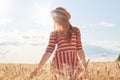 Horizontal outdoor picture of tender attractive young model looking aside, posing at wheat field, touching with hands stalks of Royalty Free Stock Photo