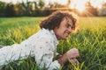 Horizontal outdoor shot of cheerful handsome young male model student with curly hair, smiling, relaxing at green lawn in the park Royalty Free Stock Photo