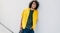 Horizontal outdoor shot of handsome smiling young man with curly hair in yellow shirt posing the city street next to the white Royalty Free Stock Photo