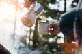 Horizontal outdoors image of young woman pours itself hot beverage in mountains near to bonfire .