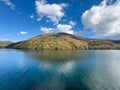 Panoramic View of a Calm Blue Lake Reflecting Forested Autumn Hills and Fluffy Clouds Royalty Free Stock Photo