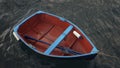 Small wooden fishing boat with a single blue oar inside, tied up near a pier against dark, murky ocean water Royalty Free Stock Photo