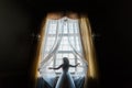 The horizontal photo of the bride touching the curtains while standing near the window.