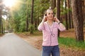 Horizontal photo of cheerful delighted good looking young female looking ahead, having headphones, listening to music, wearing