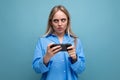 horizontal photo of a funny charming blonde girl with a grimace holding a smartphone in her hands on an isolated blue