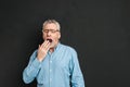 Horizontal photo of mature unshaved man 60s with grey hair wearing eyeglasses being sleepy and yawning because Royalty Free Stock Photo