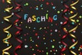 Paper streamers, confetti and letters saying carnival in German on a black background.