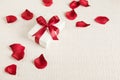 Present for Valentine`s day, Mother`s day or Wedding, wrapped in white paper, red bow and surrounded by red rose petals.