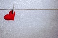 Single red heart hanging from string by clothes peg on silver background. Romantic Valentine`s Day scene with copy space