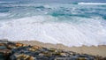 Turquoise ocean water with small white foam waves gently crashing into golden sand beach and a rocky bank Royalty Free Stock Photo