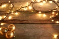 Yellow Christmas lights in rustic wooden table with golden Christmas ornaments in corner. With copy space. Royalty Free Stock Photo