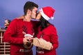 Horizontal plane of a couple wearing Christmas pajamas, exchanging gifts and kissing