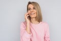 Horizontal portrait of beautiful Caucasian blonde smiling female has phone conversation, talk using modern cellphone, wears pink Royalty Free Stock Photo