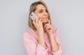 Horizontal portrait of beautiful pensive Caucasian blonde female has phone conversation, talk using modern cellphone, wears pink Royalty Free Stock Photo