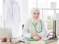 Horizontal portrait shot of an attractive smiling adult Muslim woman wearing cream hijab, stethoscope, and eyeglasses looking at Royalty Free Stock Photo