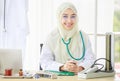 Horizontal portrait shot of an attractive smiling adult Muslim woman wearing cream hijab, stethoscope, and eyeglasses looking at Royalty Free Stock Photo