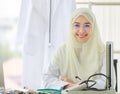 Horizontal portrait shot of an attractive smiling adult Muslim woman wearing cream hijab, stethoscope, and eyeglasses looking at Royalty Free Stock Photo